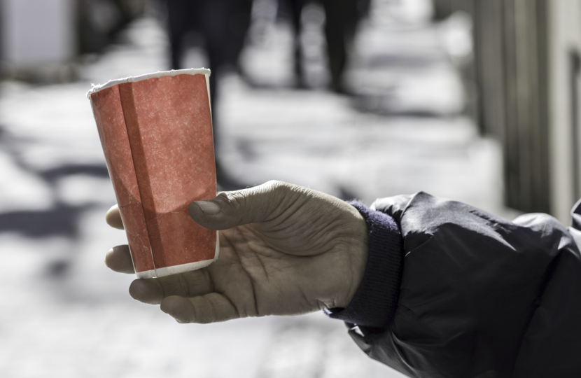 A close-up photograph captures a hand holding a small, paper cup with a hot beverage outdoors on a cold winter day, emphasizing the serenity and quiet of a chilly moment.  The scene composition centers on the hand and the cup, which are positioned in the foreground. The hand, clad in a dark jacket with a visible cuff, grips the cup gently, with fingers wrapped around its textured surface. The background is blurred, featuring snow-covered ground and indistinct figures or objects