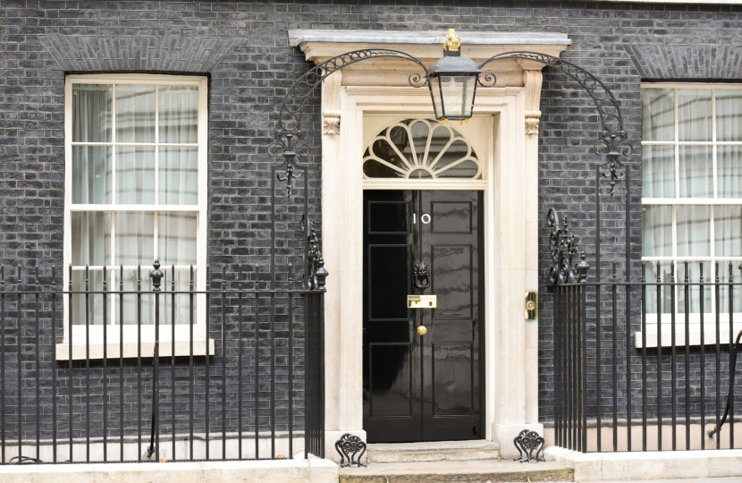 A black front door with the number 10, set in a white stone frame with a fanlight window above. The building features dark brick walls, two barred windows, and iron railings.