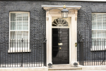 A black front door with the number 10, set in a white stone frame with a fanlight window above. The building features dark brick walls, two barred windows, and iron railings.