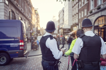 Two police officers in uniform stand on a busy city street near a police van, while pedestrians walk along the cobblestone road—capturing a typical day in the Westminster City Council area.